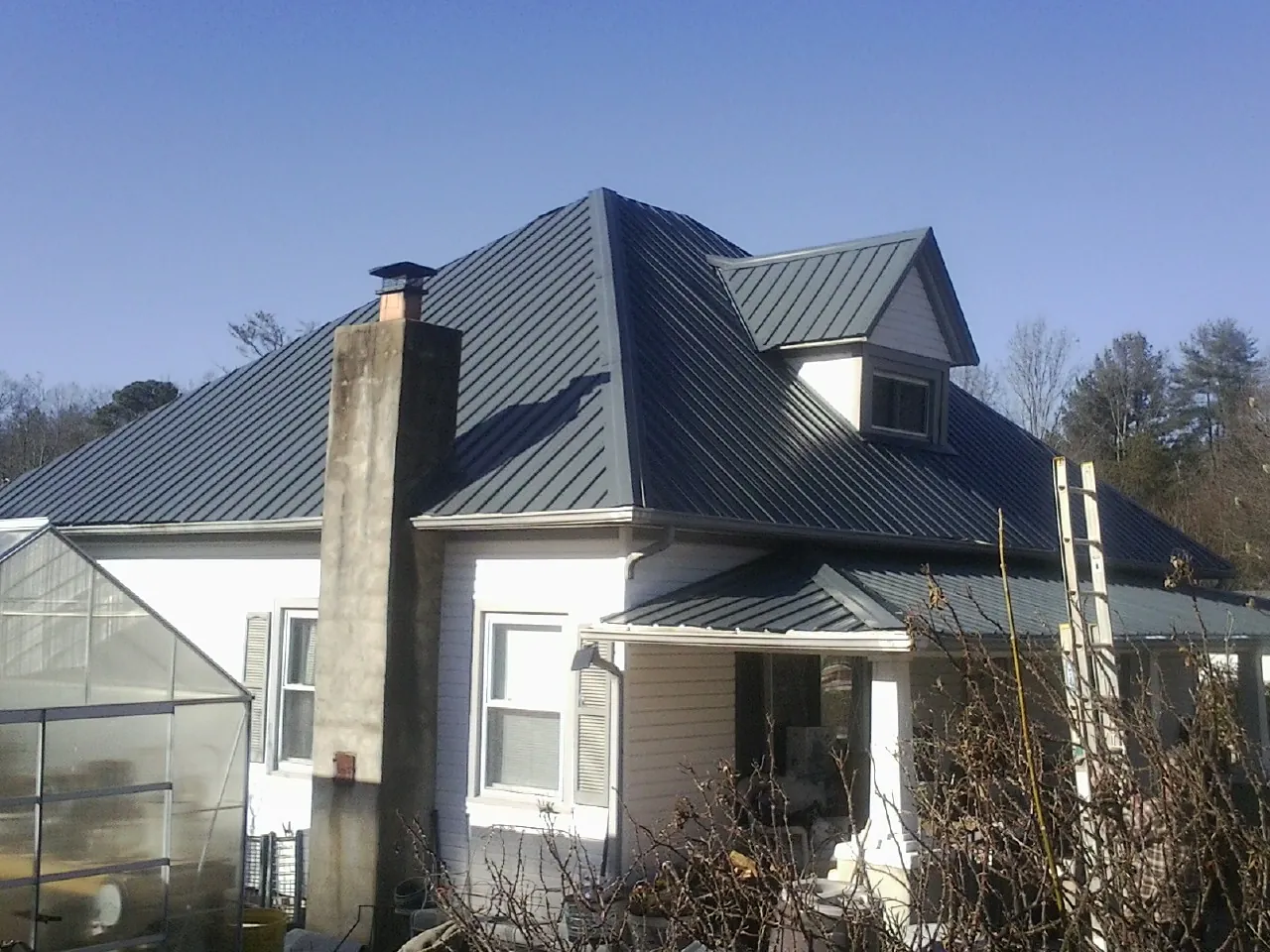Dark blue standing seam metal roof on a white farmhouse with dormer — Slate & Tile Roof Repair by Roofing Brothers in Stanfield