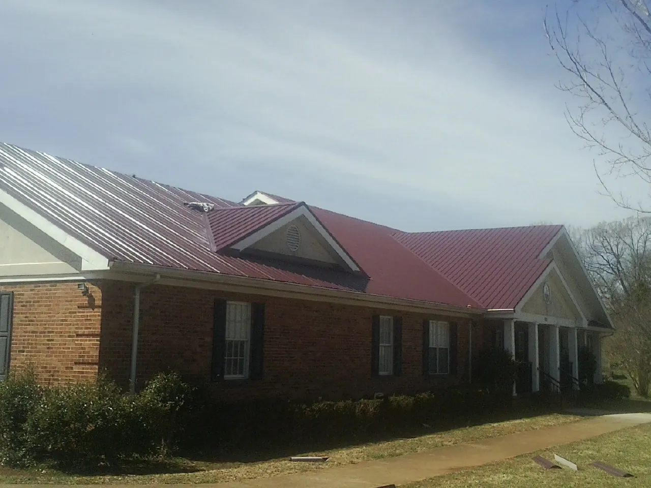 Red metal roof with gabled entries on a long brick building, from a Hail Damage Roof Repair job in Stanfield