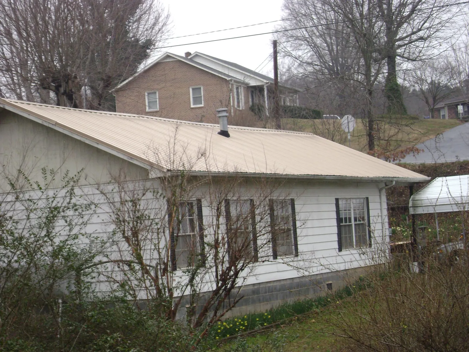 Tan metal roof on a white sided house set into a hillside — Commercial Roofing by Roofing Brothers in Stanfield